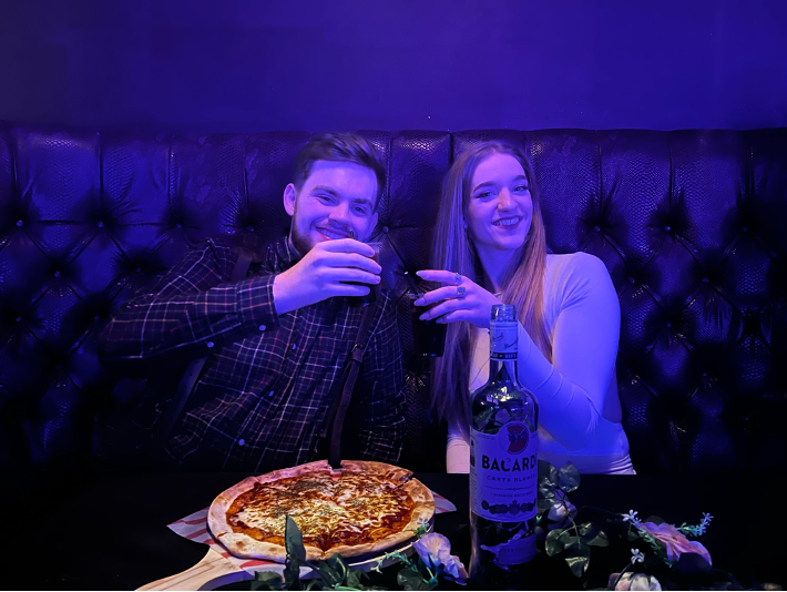 A couple sitting around a table with pizza and holding glasses