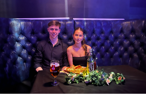 A couple sitting around a table with drinks and pizza